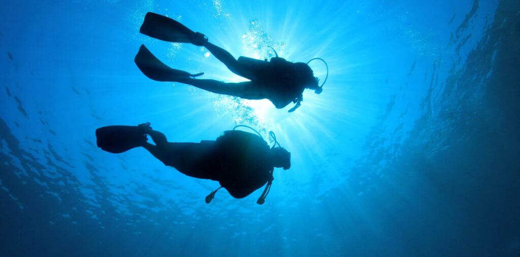 Dos buceadores en contraluz bajo el agua. Imagen artística de submarinismo.