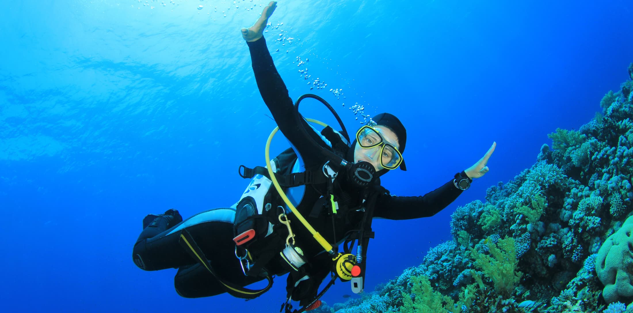 Buceadora sonriendo bajo el agua rodeada de peces. Fotografía de buceo recreativo.