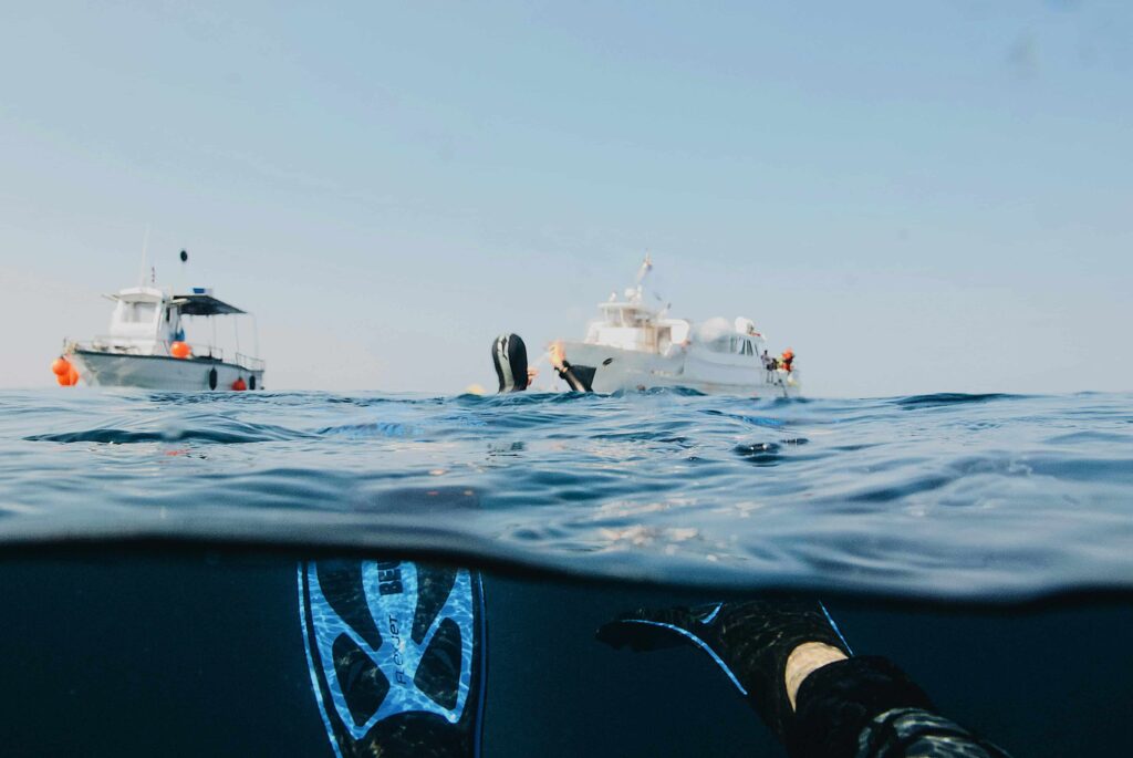 Apneísta nadando en mar abierto cerca de un barco. Freediving en aguas cristalinas.