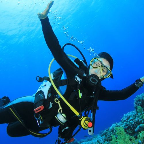 Buceadora sonriendo bajo el agua rodeada de peces. Fotografía de buceo recreativo.